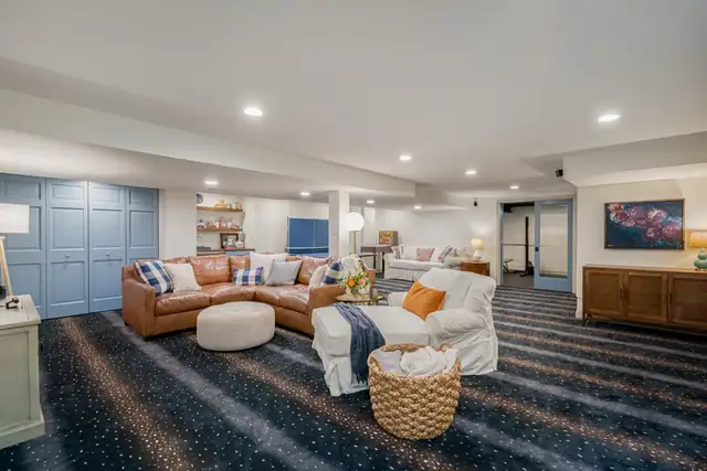 Finished basement on Riveredge Court with leather sectional, blue paneled wall, built-in shelving and patterned carpet