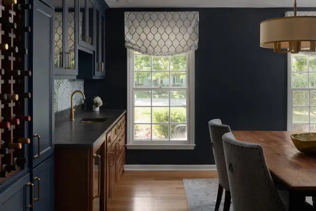 Navy dining room with a built-in bar, wine storage, brass pendant and a window with a patterned Roman shade