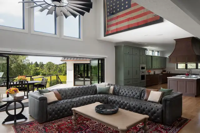 Open great room with a tufted leather sectional, green kitchen cabinets beyond and a wall of glass doors open to the patio