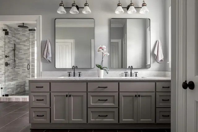 Bathroom with a gray double vanity, black hardware, twin mirrors, schoolhouse sconces and a tiled walk-in shower
