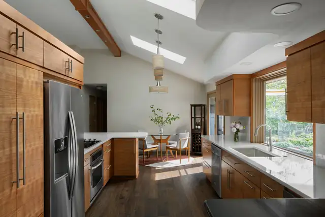 River Road kitchen with warm wood cabinetry, vaulted ceiling with beam and skylight, and a window over the sink