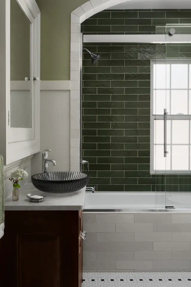 Bathroom with arched opening, deep green subway tile shower surround, white wainscoting and vessel sink