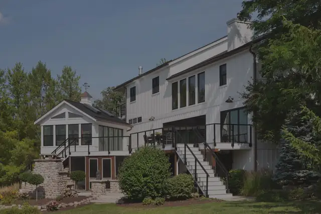 Rear of a white two-story home with a screened porch addition, stone retaining wall and black deck railings