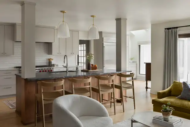 Open kitchen and living area with dark stone peninsula, wood bar stools, brass pendants and white subway tile